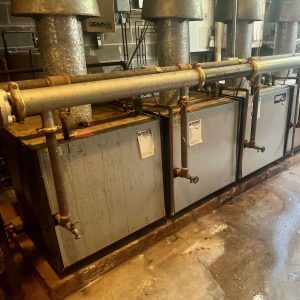 Boiler repair and servicing equipment in a workshop, showcasing multiple boiler units with pipes and valves, representing Kelly Boiler's commitment to quality service.